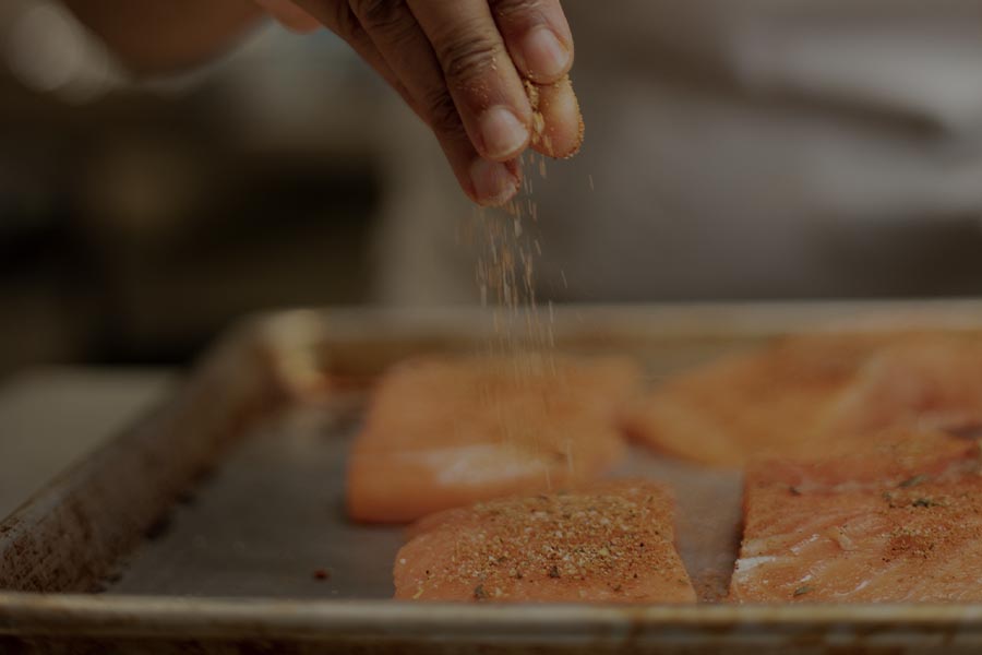 person seasoning salmon on a pan